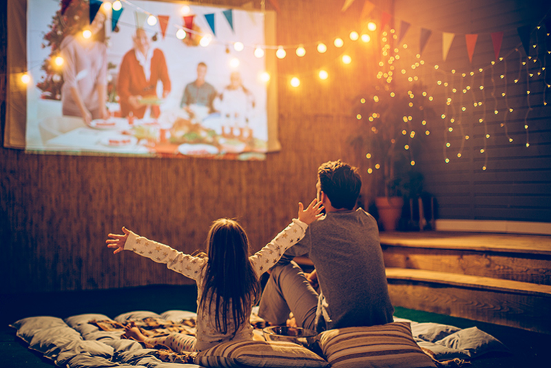 Father and daughter watching movie projected on wall outside
