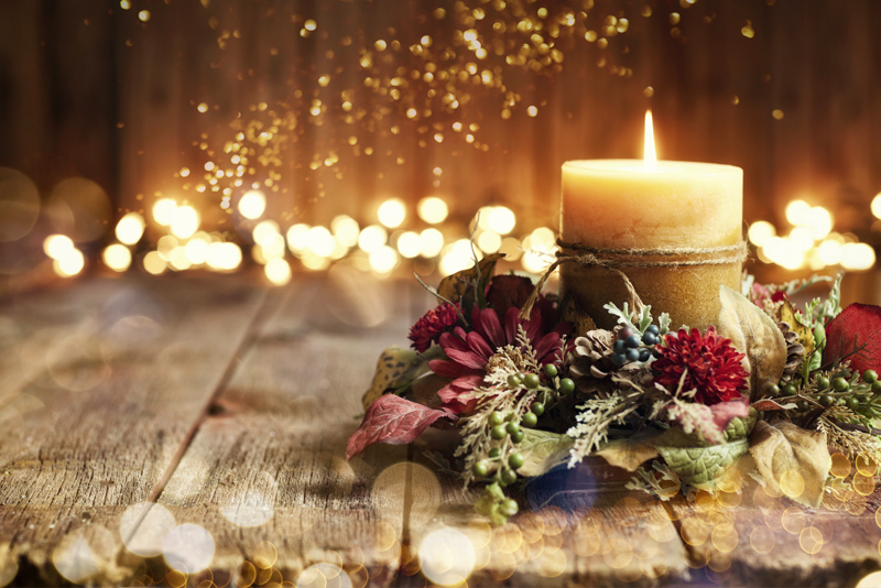 Holiday candle on wood table with holiday lights in background