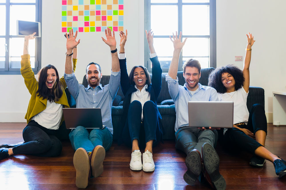 Smiling group of people sitting on wood floor.