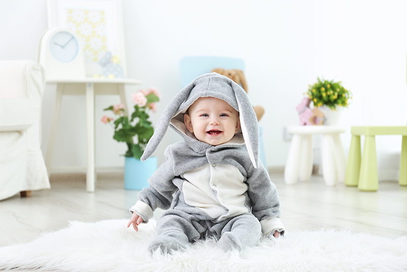 Cute little baby in bunny costume sitting on furry rug at home