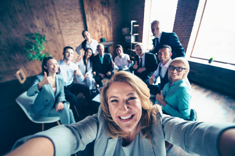 Happy business woman taking selfie with coworkers.