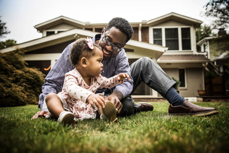 Happy man and baby daughter playing on front lawn.