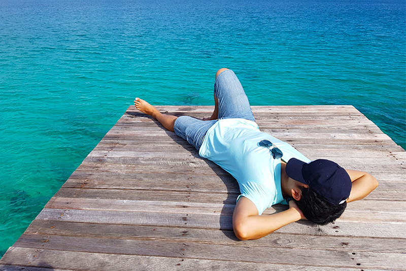 Young man lying down on wooden pier near the sea