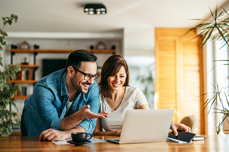 Smiling couple looking at laptop together at cozy home office