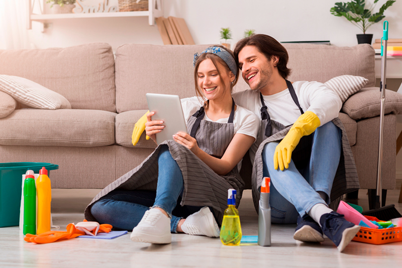 Happy couple sitting on floor with cleaning supplies