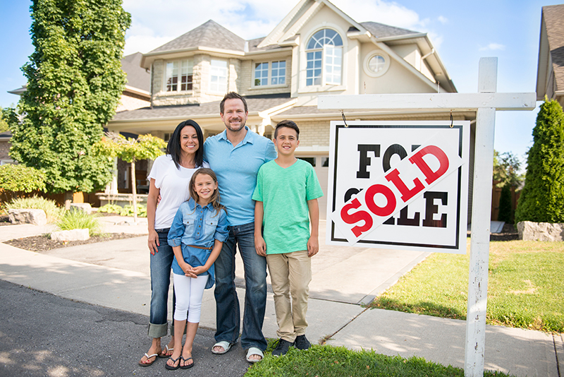 Happy family standing in front of house with sold sign