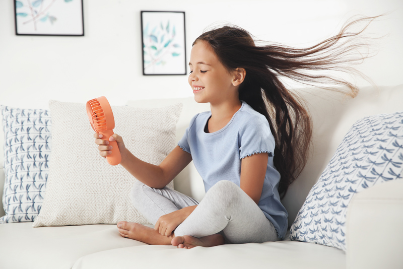 Young girl sitting on couch with handheld fan