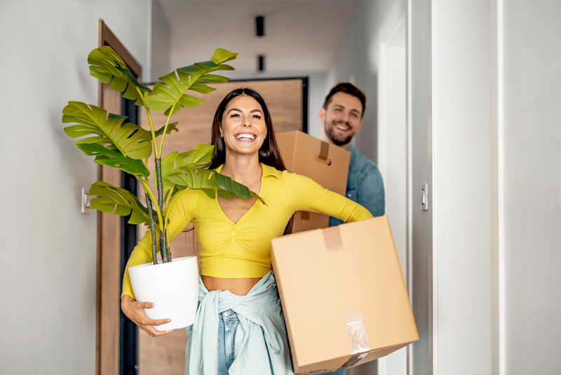 Happy couple carrying a plant and moving boxes