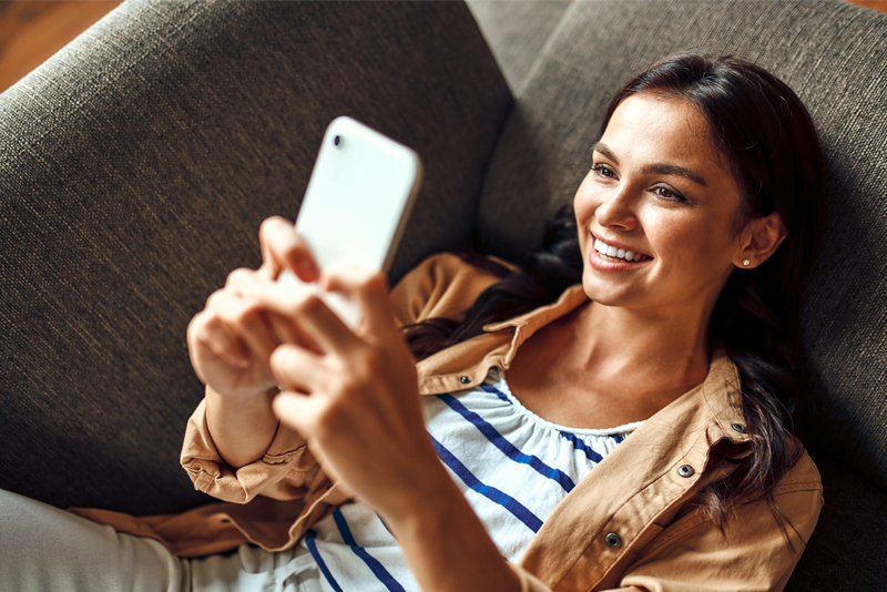Excited young woman sitting on couch with mobile phone Excited young woman sitting on couch with mobile phone