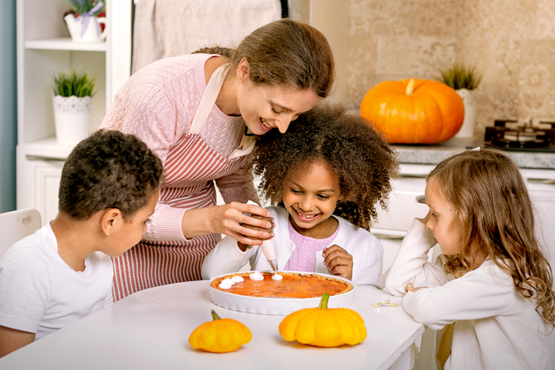 Happy mom and kids decorating a pumpkin pie