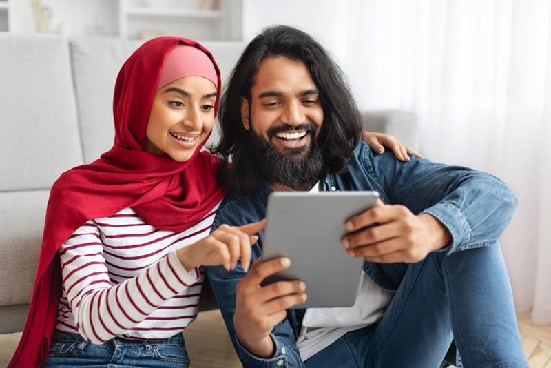 Excited couple sitting in living room with tablet