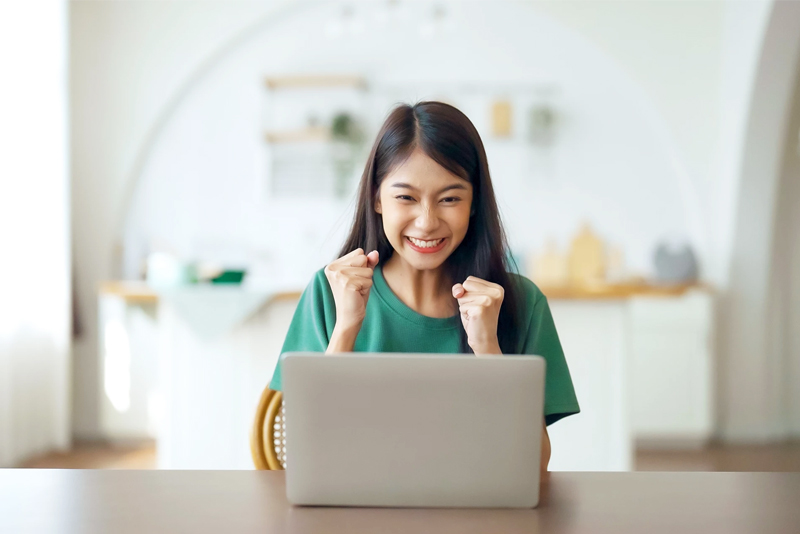 Excited young woman sitting at kitchen table with laptop