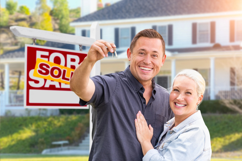 Happy couple holding house keys in front of house sold sign