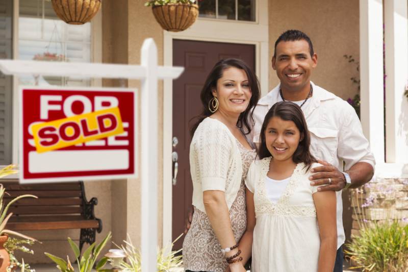 Happy family of three standing in front of house with sold sign 800x534