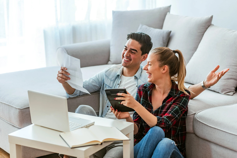 Happy couple sitting on living room floor with laptop and calculator