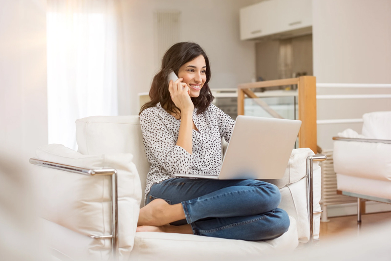 Young woman takling on phone while working on laptop