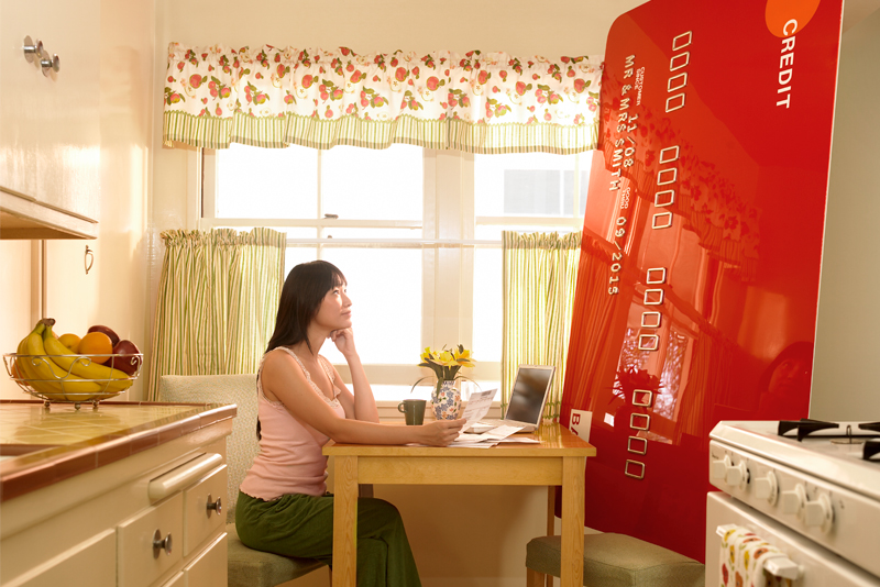 Woman sitting at kitchen table with giant credit card