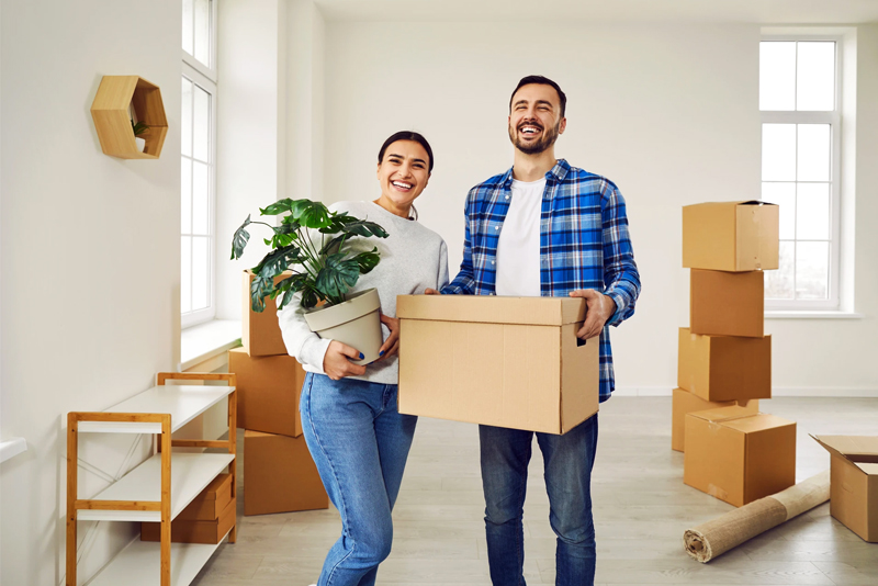 Happy couple carrying plant and box into new home