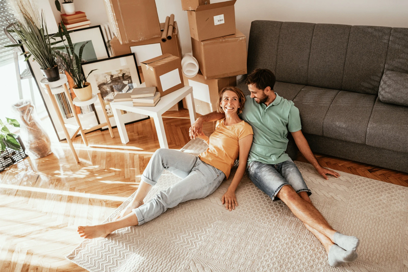 Happy man and woman sitting on living room floor with moving boxes